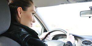 A woman glances in the rearview mirror as she drives her car on a sunny day.